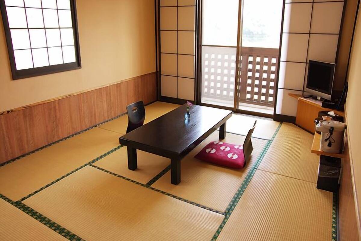 A traditional tatami mat room with a low table, chairs, a television, and sliding doors.