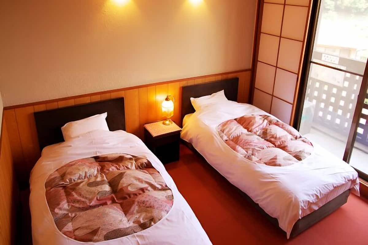A hotel room with two beds, a nightstand with a lamp, and a sliding glass door to the outside.