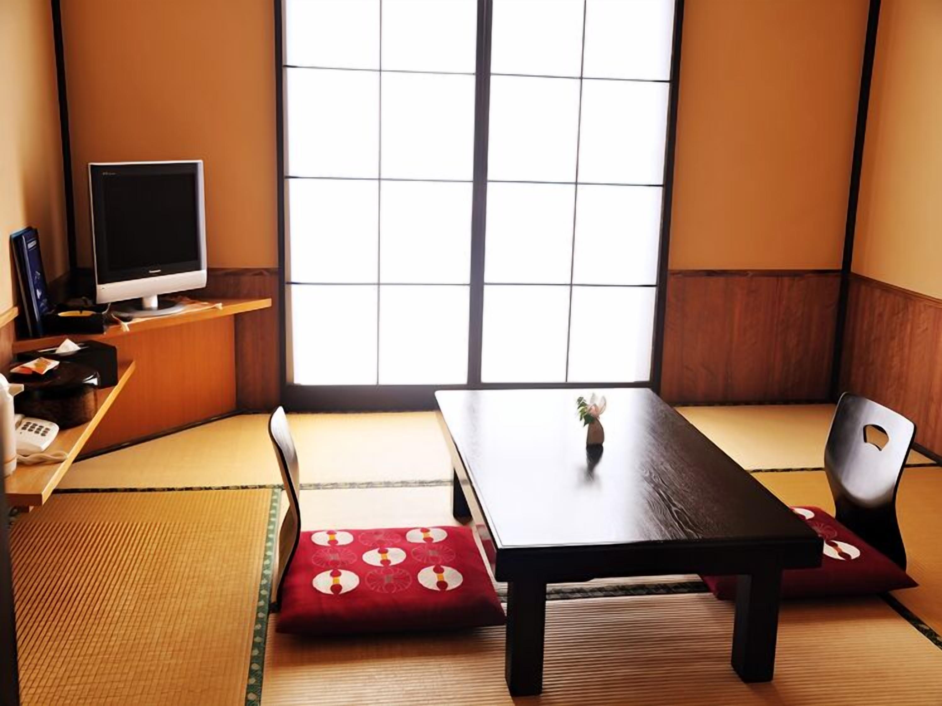 Une pièce de style japonais traditionnel, avec un sol recouvert de tatamis, une table basse, une chaise et un téléviseur posé sur une étagère.