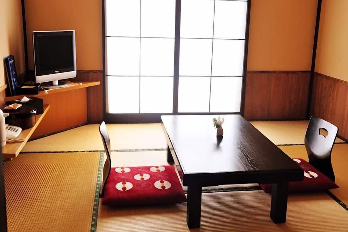 A traditional Japanese room with tatami flooring, a low table, a chair, and a television on a shelf.
