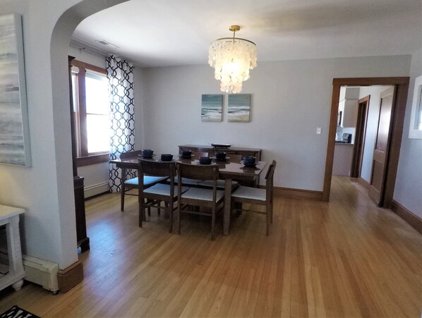 A dining area with a wooden table and chairs, a chandelier, and artwork on the wall. - Sea Level Sanctuary's High Tide (Seaside Park)