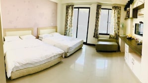 Habitación de hotel con dos camas, una zona de estar pequeña, televisión y balcón con cortinas.