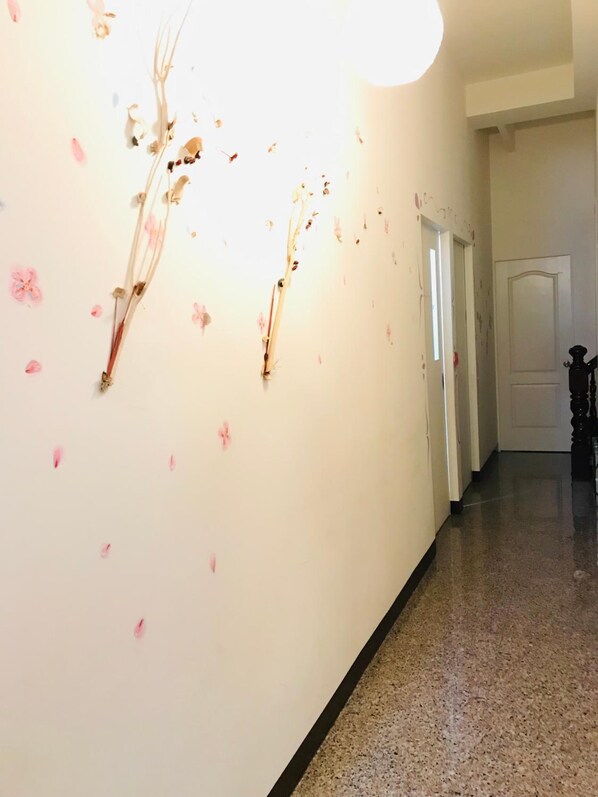 Un pasillo con piso pulido, pared blanca con adornos florales y una puerta al final.
