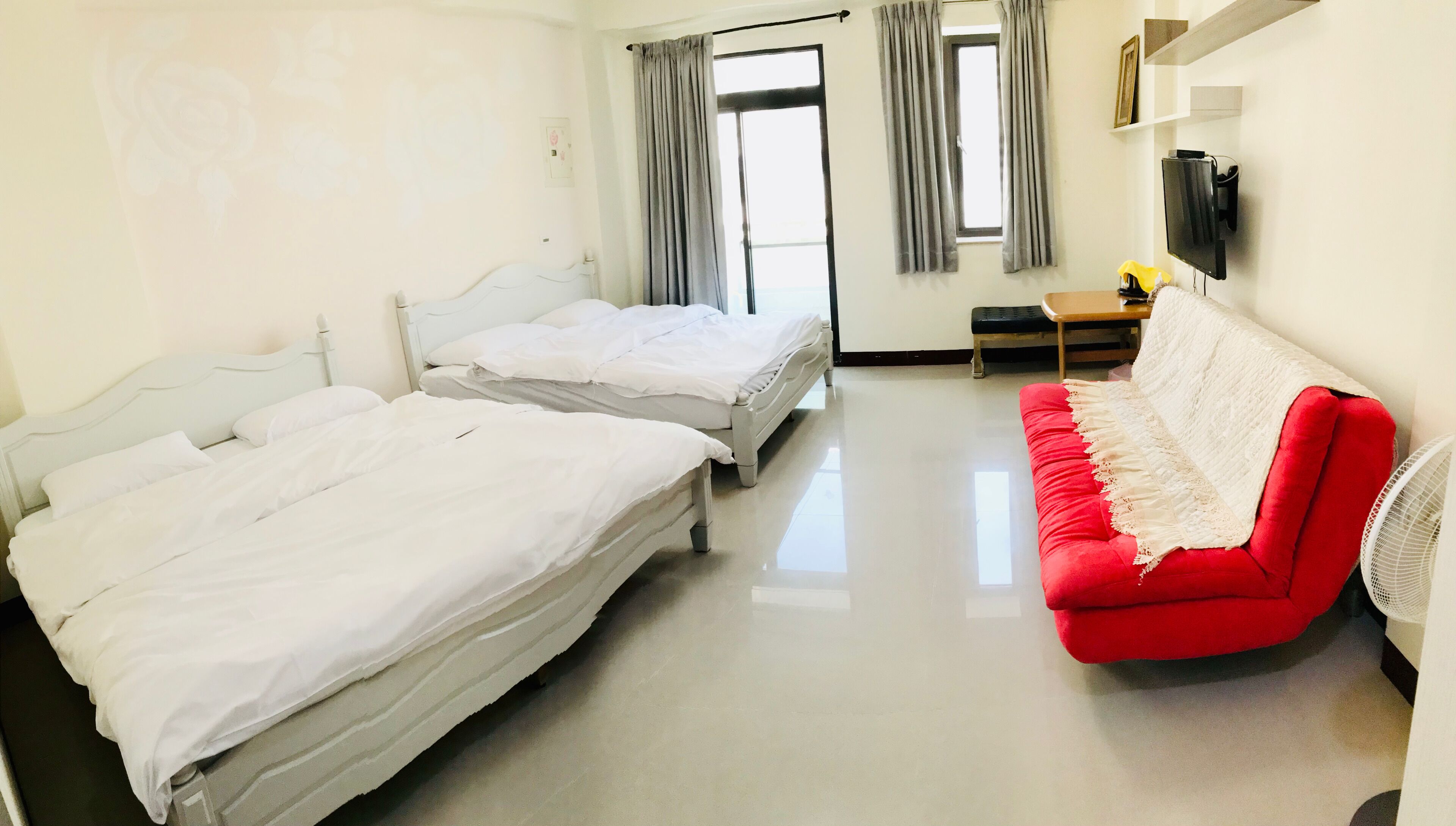 Habitación de hotel con dos camas, un sofá rojo, una mesita y un televisor.