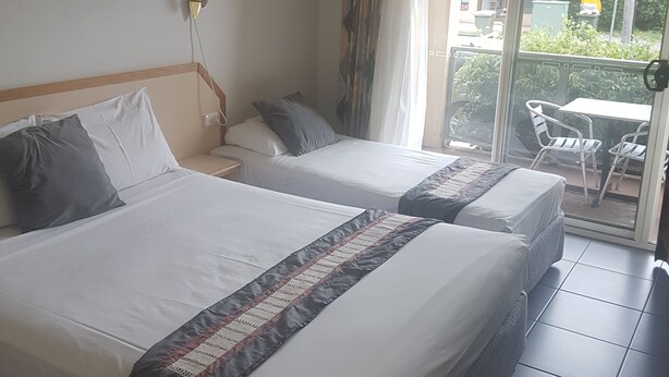 A hotel room with two beds, a window with curtains, an air conditioning unit, and a view of the outside balcony area. - Jopen Cafe & Motel (Sussex Inlet)