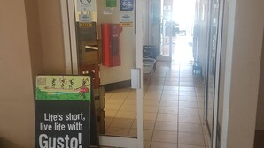 A hallway with a sign that reads "Life's short, live life with Gusto!" and a door with various signs including "NO SMOKING" and "8.2". - Jopen Cafe & Motel (Sussex Inlet)