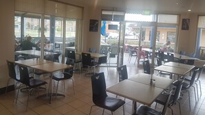 A restaurant with indoor seating, large windows, and an exit sign. - Jopen Cafe & Motel (Sussex Inlet)