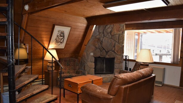 Un salón acogedor con chimenea de piedra, escalera de madera, sofá de cuero y una obra enmarcada en la pared.