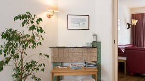 A room with a wooden table, two white stools, a potted plant, a bulletin board, and a framed picture on the wall.