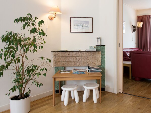 Una habitación con una mesa de madera, dos taburetes blancos, una planta en maceta, un tablón de anuncios y un cuadro en la pared.