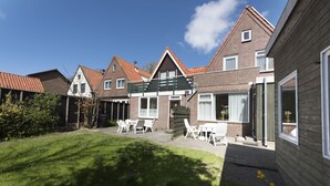 A residential building with a brick facade, a wooden deck, and a small garden area with outdoor furniture.