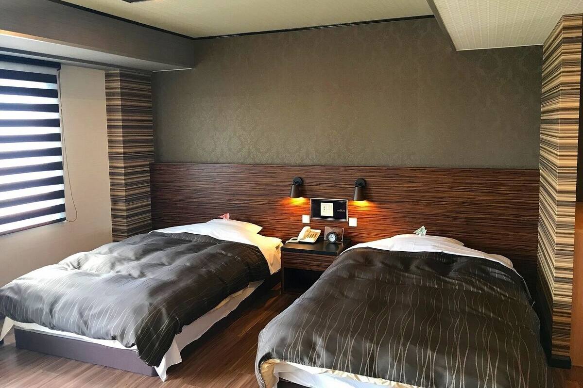 Een hotelkamer met twee bedden, een nachtkastje met telefoon en klok, en een wandlamp.
