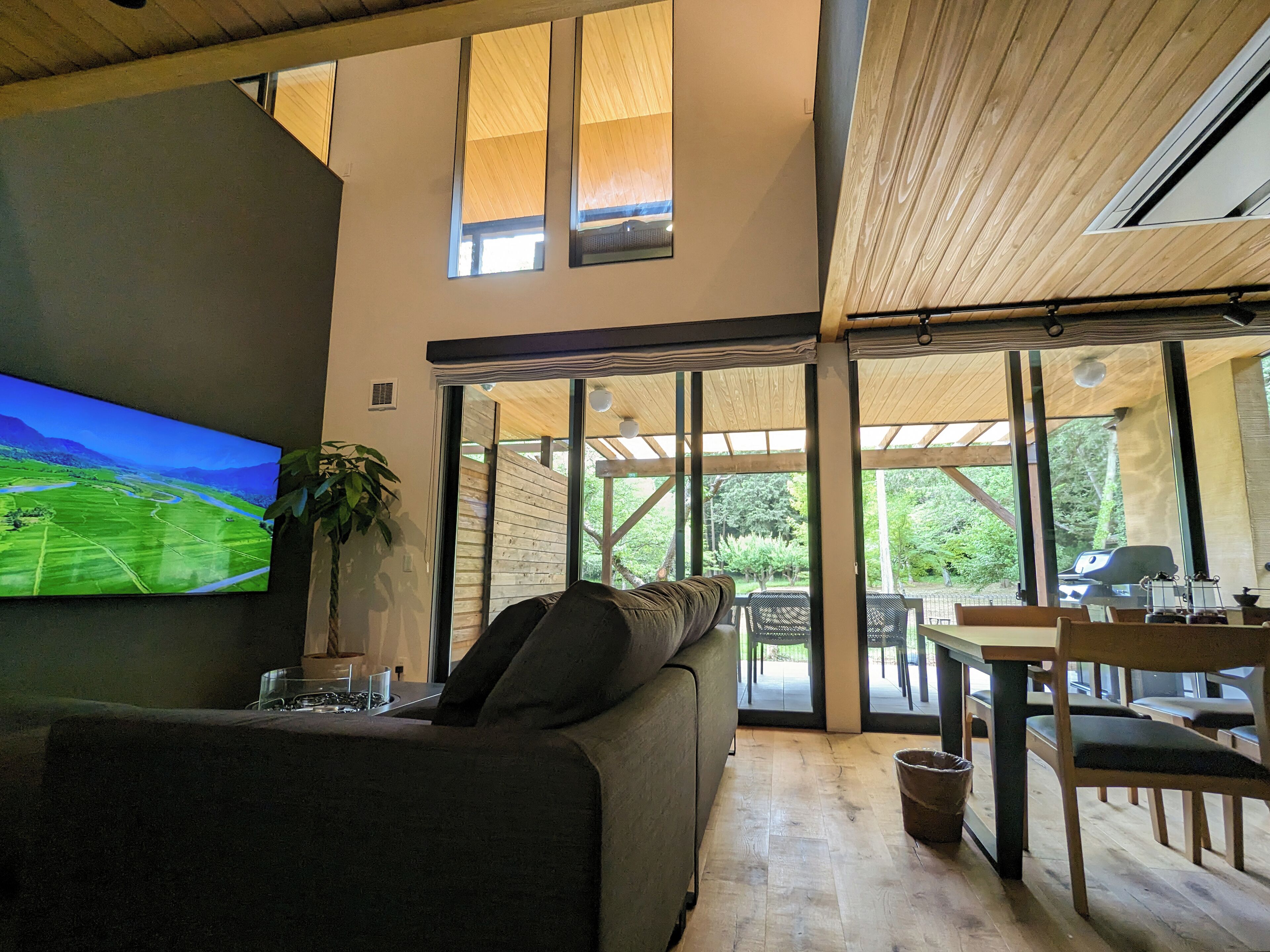 A modern living room with a large flat-screen TV, a sofa, and a dining area with wooden furniture.