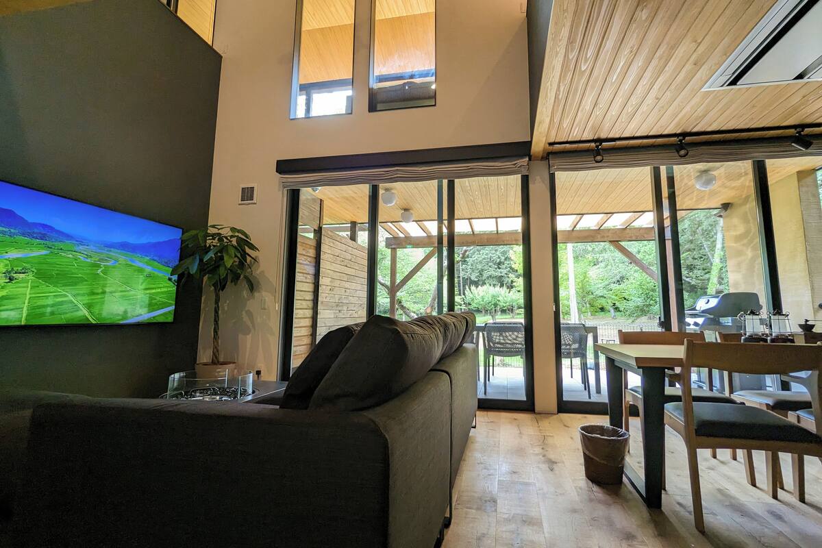 Een moderne woonkamer met een grote flatscreen televisie, een bank en een eethoek met houten meubels.