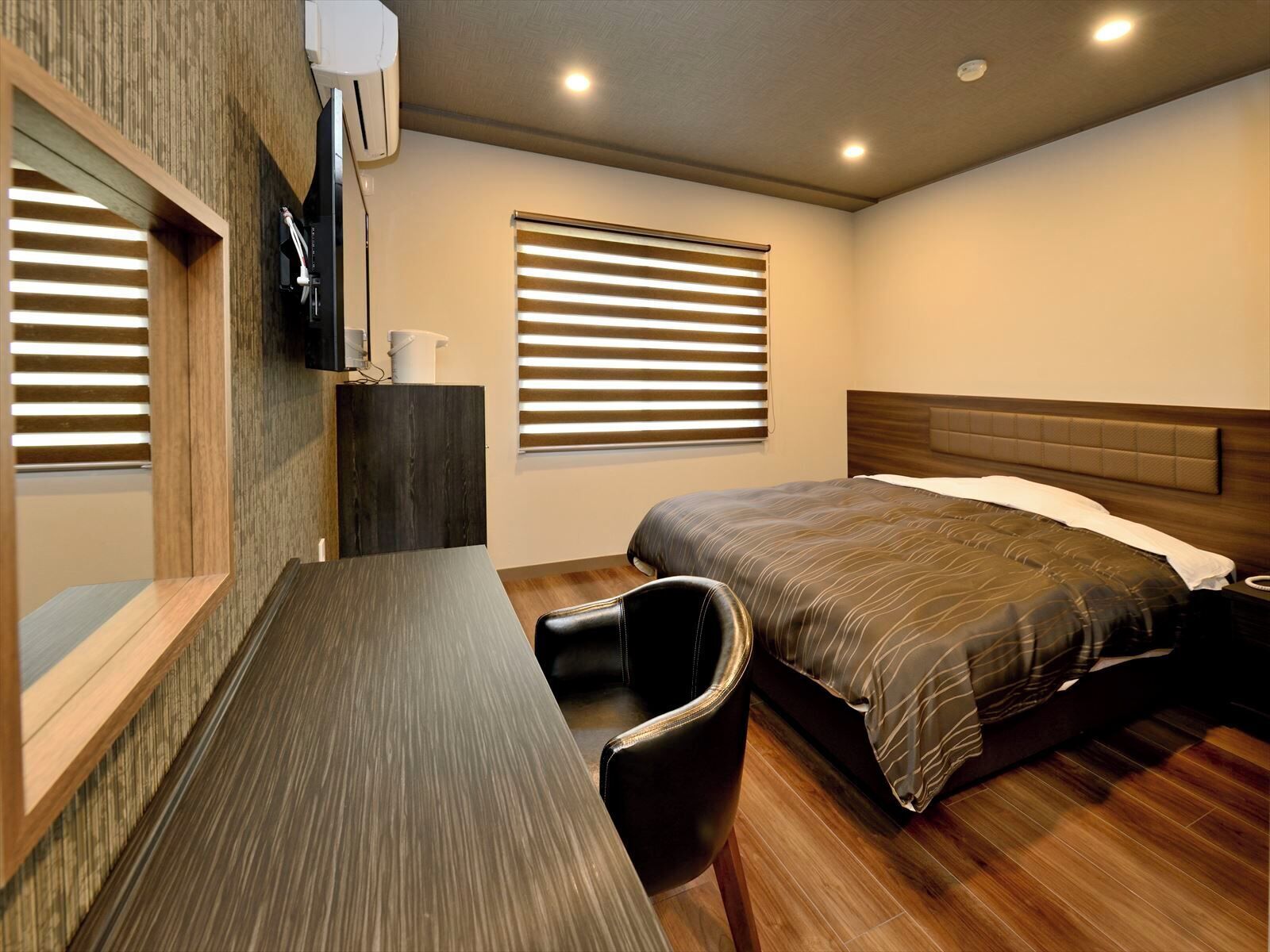 A bedroom with a bed, a desk, a chair, a TV, and a window with blinds.