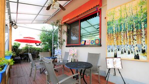 Une terrasse extérieure avec un plancher en bois, des chaises en métal, une table ronde et un auvent rouge.