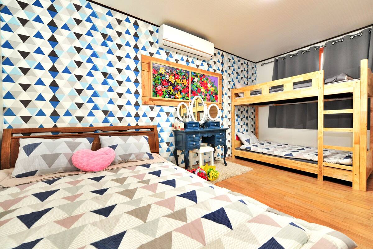 Ein Schlafzimmer mit Wand im geometrischen Muster, einem Etagenbett, einem Schreibtisch mit Spiegel und einem Bett mit gemustertem Überwurf.