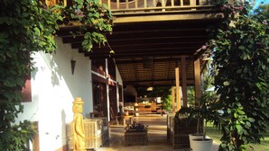 A covered outdoor seating area with wicker furniture, a statue, and potted plants.