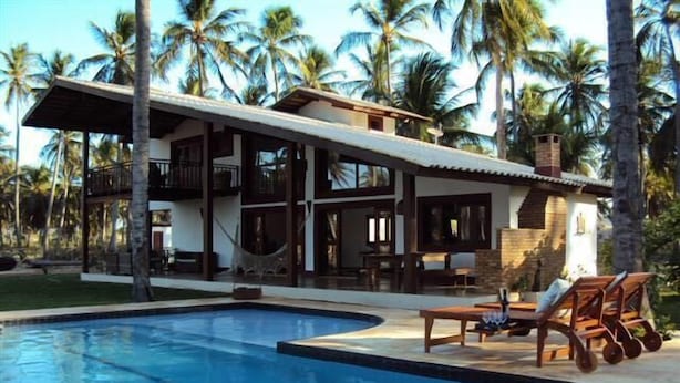 A two-story house with a swimming pool, surrounded by palm trees.