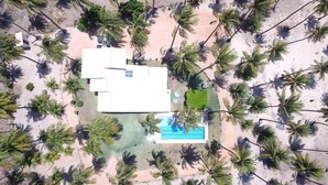 An aerial view of a resort with a swimming pool, multiple buildings, and palm trees.