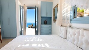 A bedroom with a bed, a dresser, and a view of the sea.