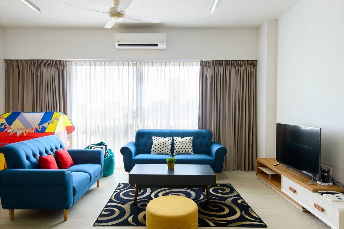 Una sala de estar moderna con un sofá azul, un otoman amarillo, una mesita de centro y un televisor.