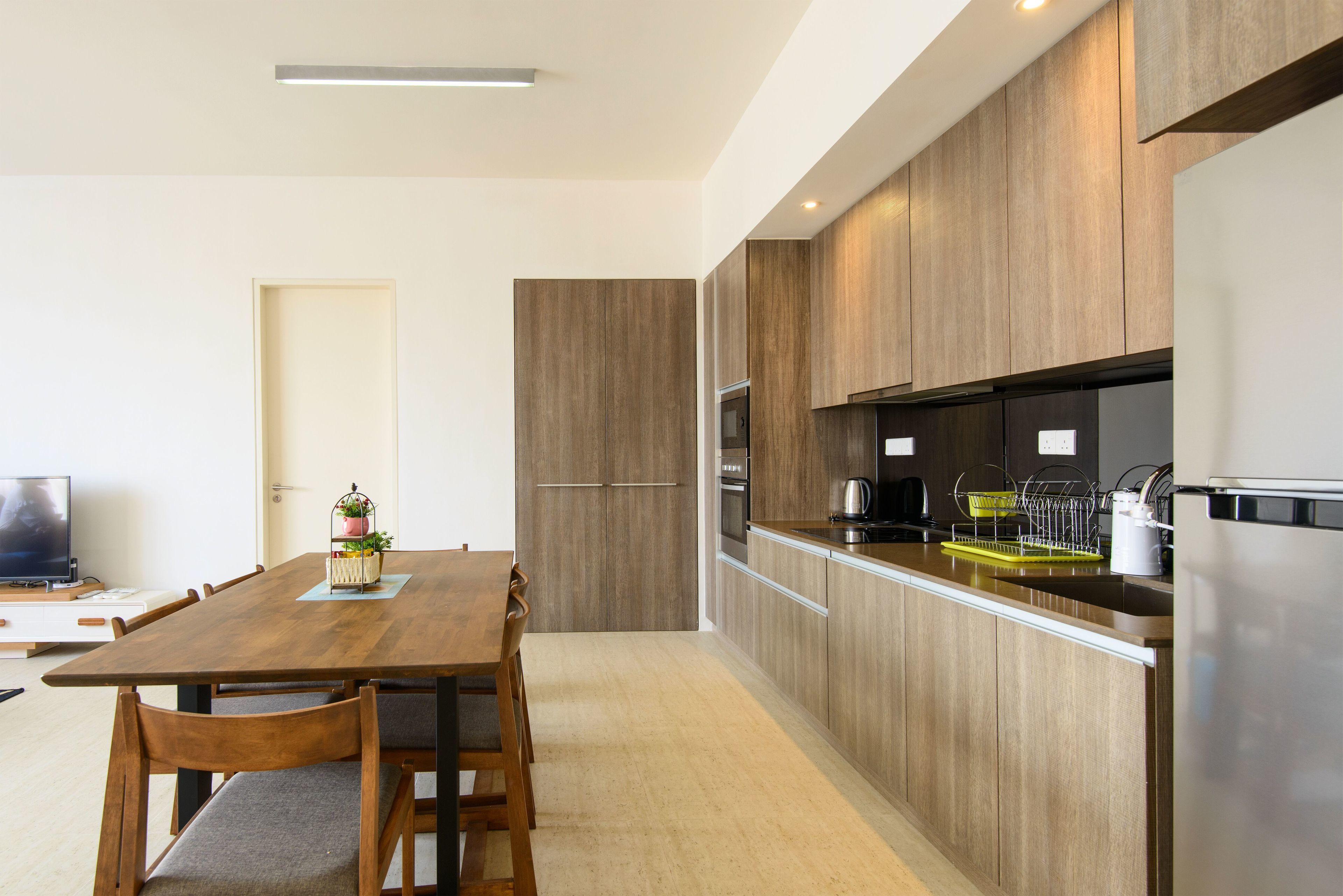 A modern kitchen with wooden cabinets, a stainless steel refrigerator, and a dining area with a wooden table and chairs.