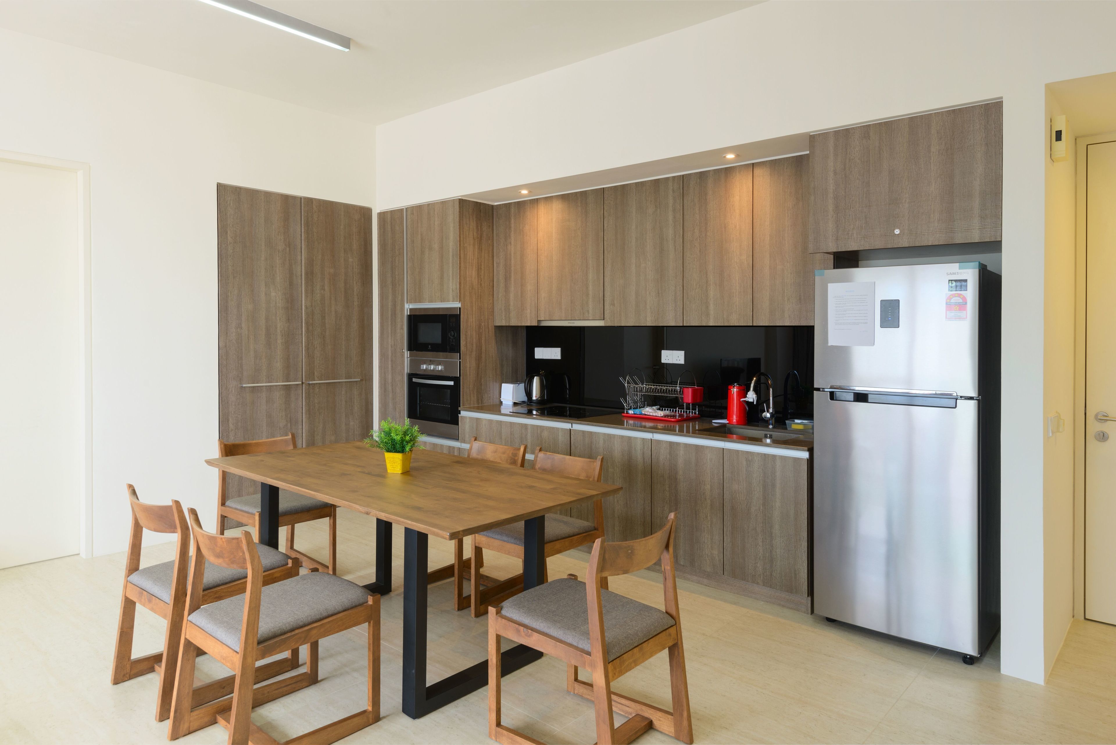 A modern kitchen with wooden cabinetry, a stainless steel refrigerator, and a dining area with a wooden table and chairs.
