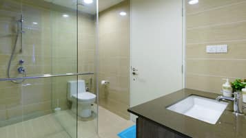 A modern bathroom with a glass shower enclosure, a white toilet, and a sink with a dark countertop.