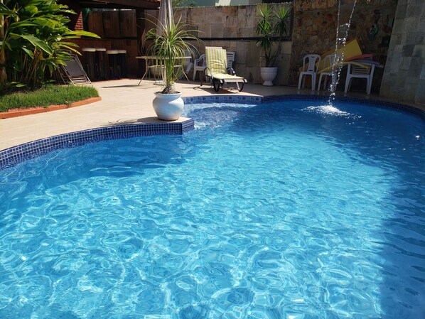 A clear blue pool with a tiled edge, surrounded by lounge chairs and potted plants.