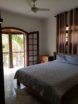 A bedroom with a bed, a wooden nightstand, a ceiling fan, and a view of a garden through a glass door.