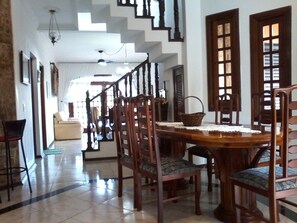 A dining area with a wooden table and chairs, a staircase, and a sofa in the background.