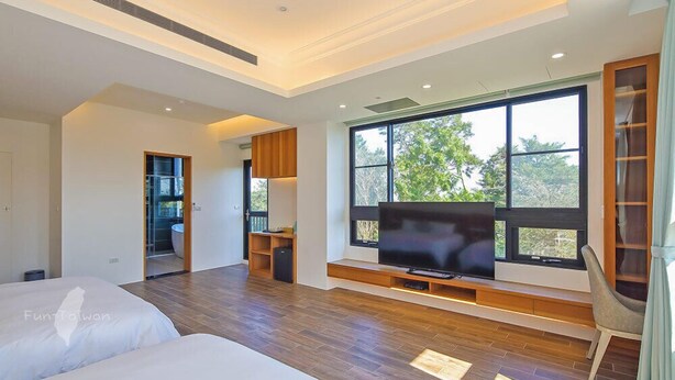 A modern bedroom with a large TV, wooden flooring, and a view through the window. - Monet Garden B&B (Wujie)