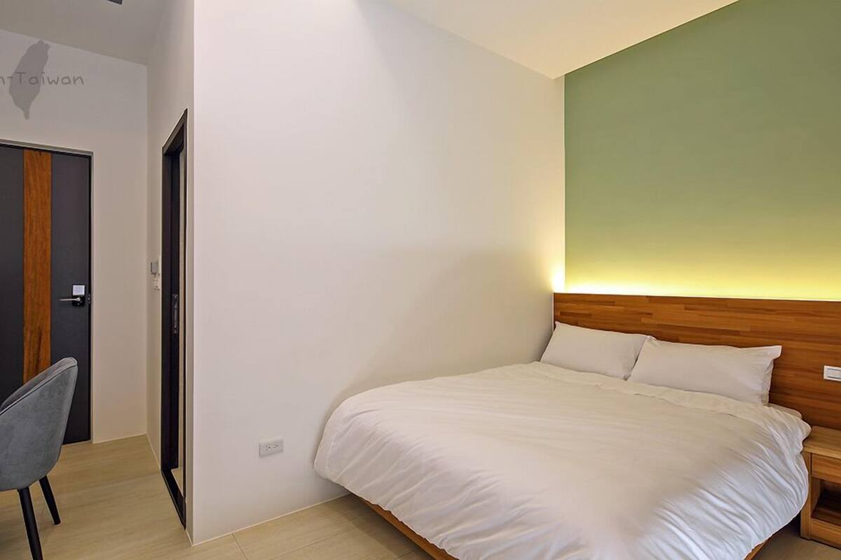 Un dormitorio con una cama, una silla, una puerta y una pared con una lámpara.