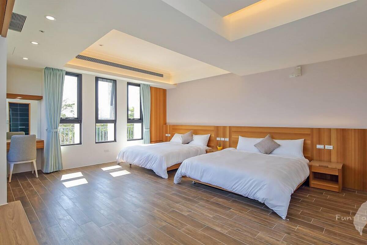 Una habitación de hotel moderna con dos camas, un escritorio y ventanas amplias.