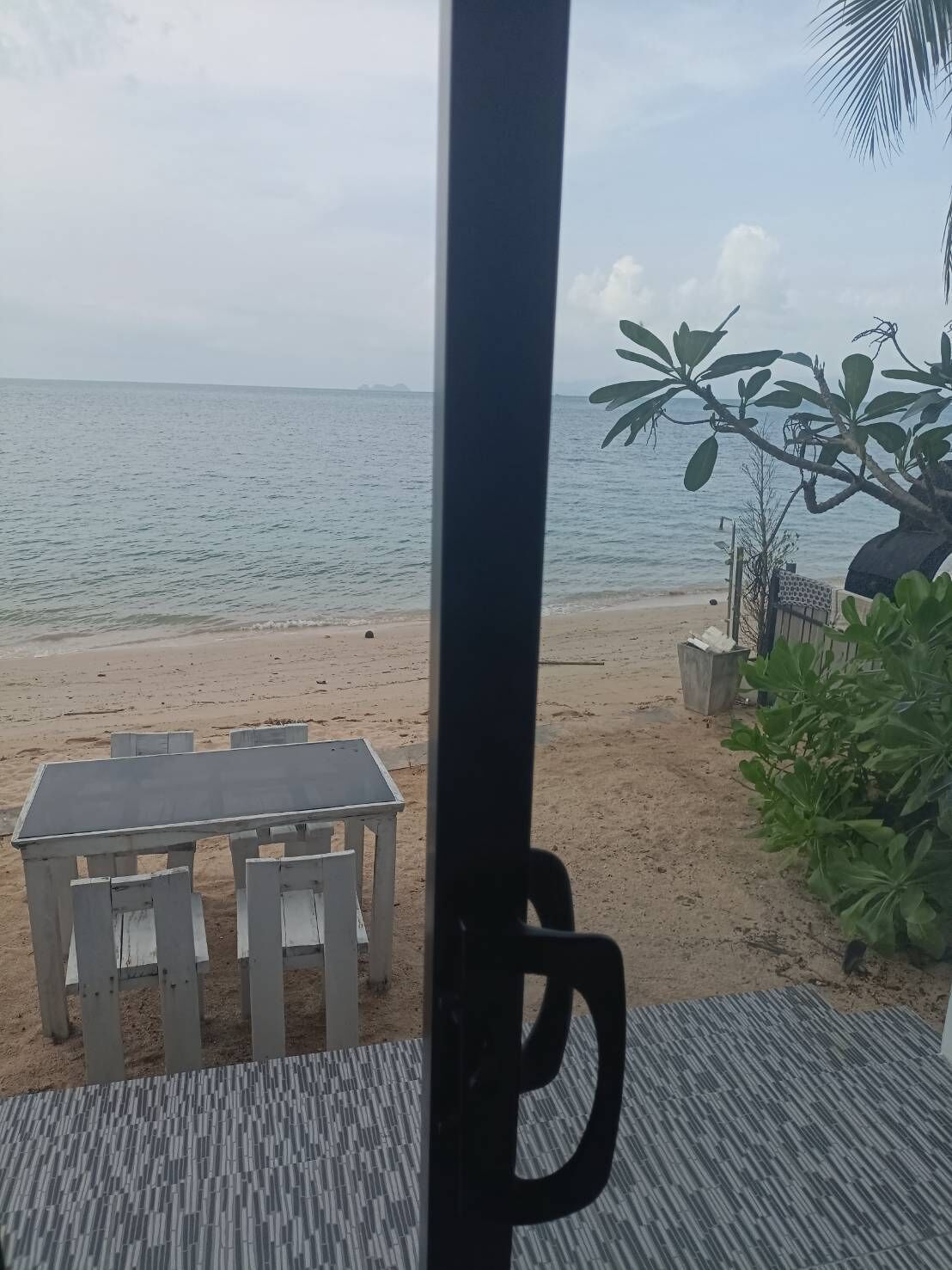 A beach view with a table and chairs, a palm tree, and a bench.