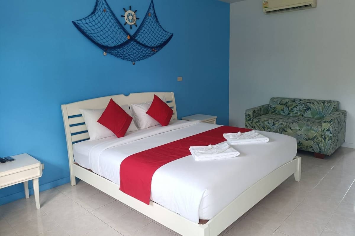 Quarto com cama, mesa de cabeceira, sofá verde estampado e um objeto decorativo na parede.