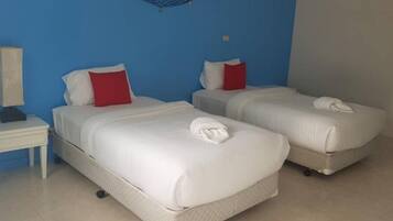 Een hotelkamer met twee bedden, elk voorzien van witte lakens en rode kussens. Er is een klein nachtkastje met een lamp en een wandplank boven de bedden.