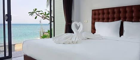 A hotel room with a large bed, a view of the ocean, and a tropical plant.