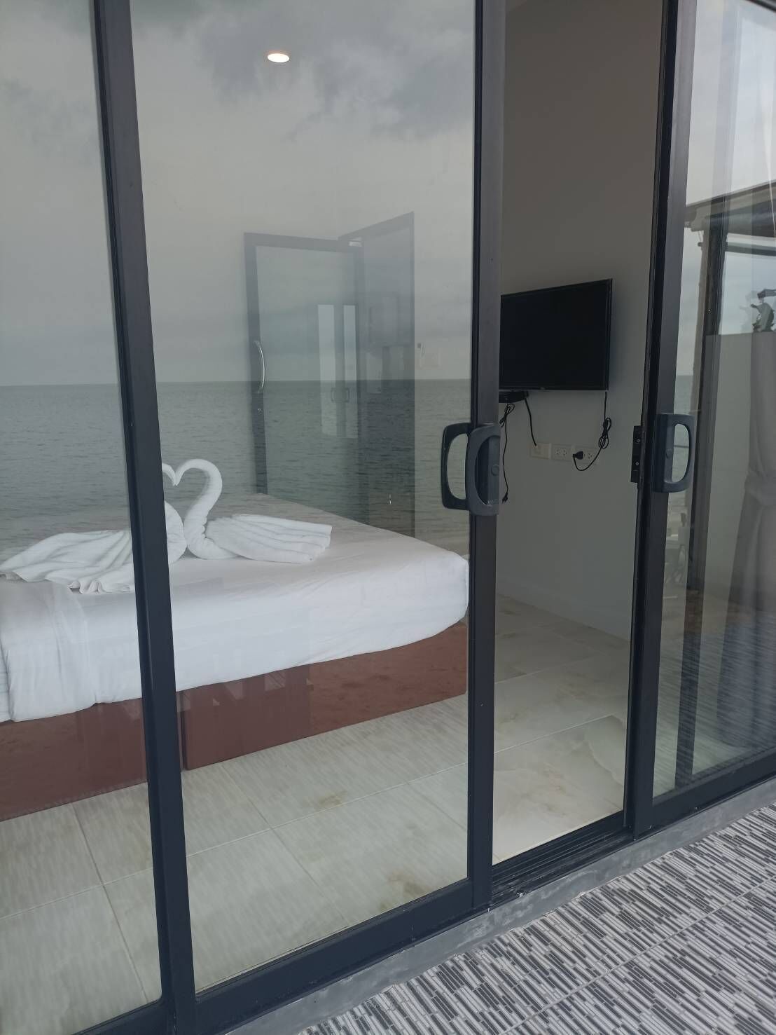A bedroom with a bed, a TV, and a view of the sea through a glass door.