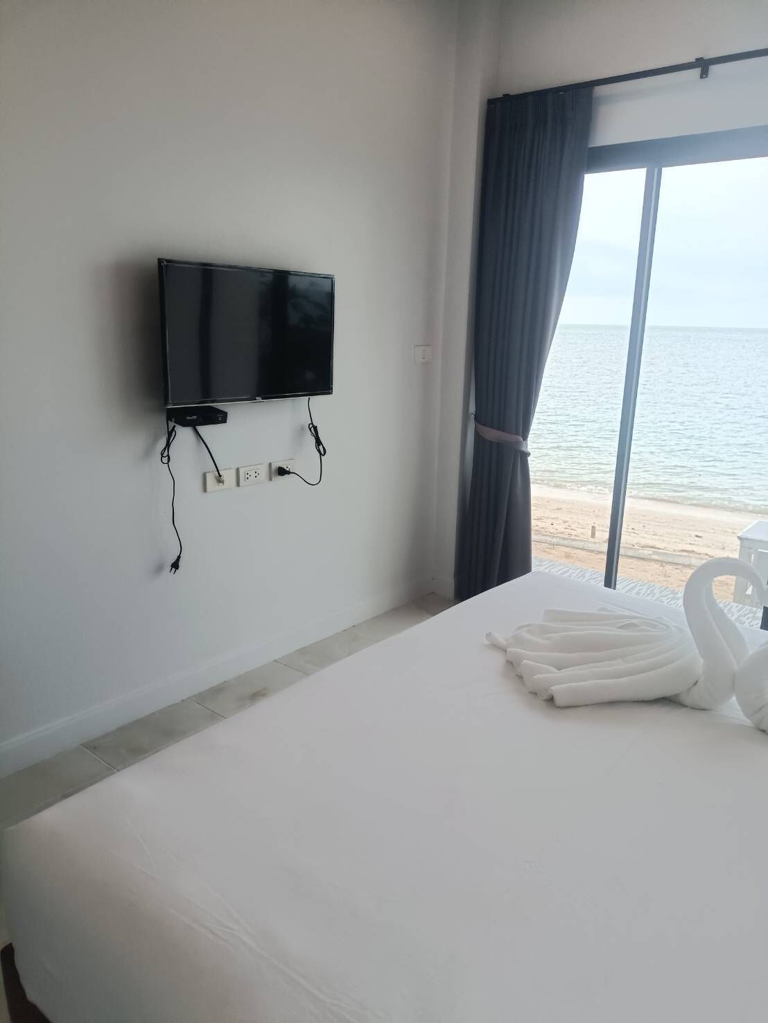 Een hotelkamer met een bed, een flatscreen televisie aan de muur en uitzicht op zee door een groot raam.