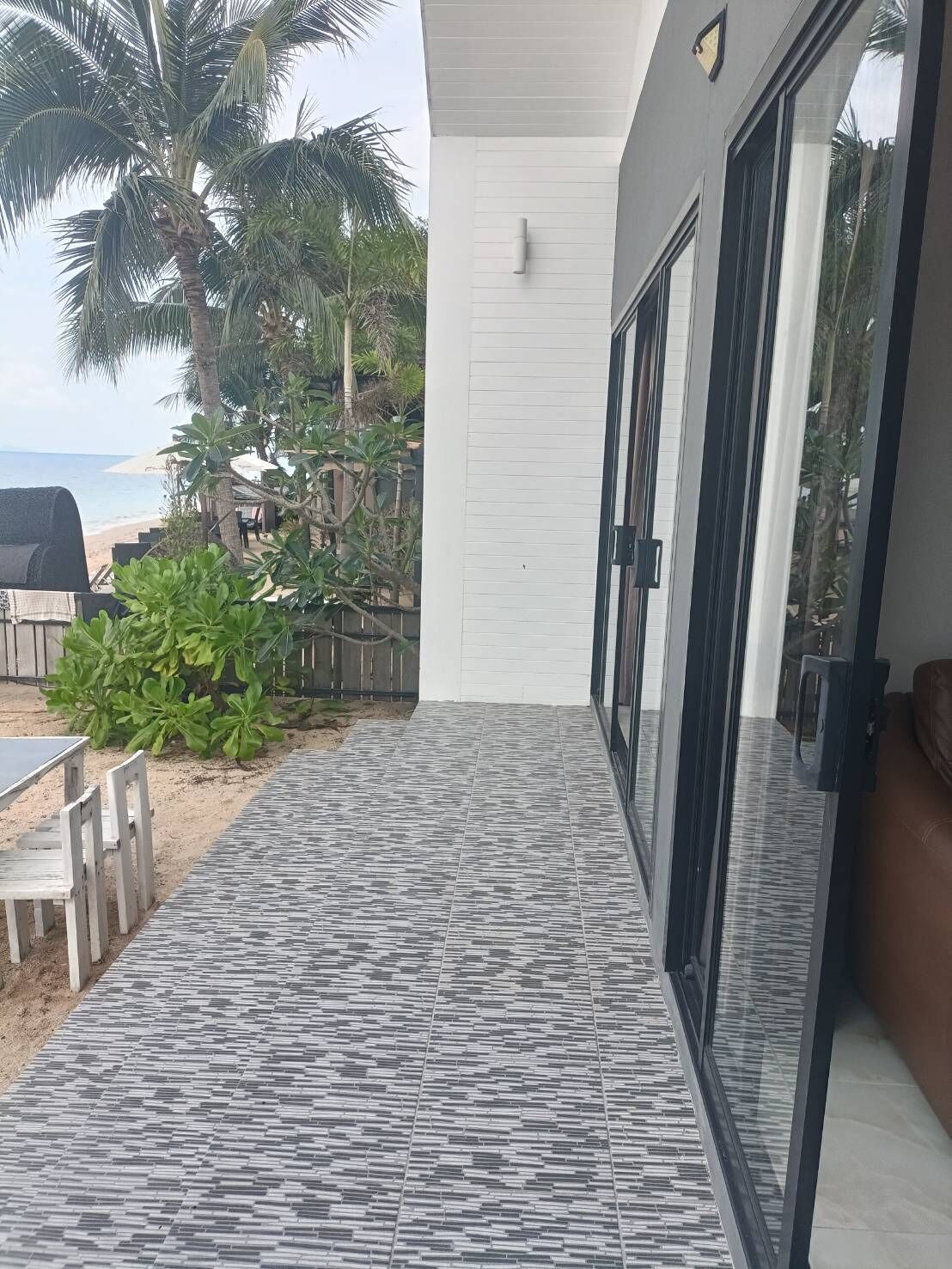 A covered outdoor area with a tiled floor, a wooden table, and chairs, leading to a glass door.