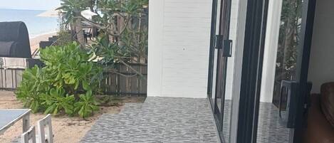 A covered outdoor area with a tiled floor, a wooden table, and chairs, leading to a glass door.