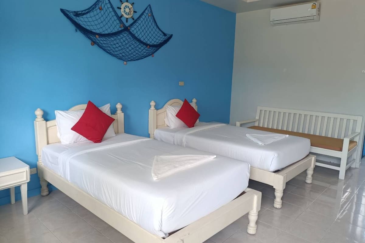 Quarto de hotel com duas camas, cada uma com roupa de cama branca e almofadas vermelhas, parede azul com uma rede decorativa e radiador branco.