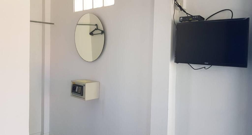 A room with a flat-screen TV mounted on the wall, a round mirror, and a small control panel.