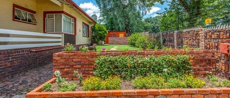 A residential property with a brick garden, a wooden fence, and a house with a red roof.