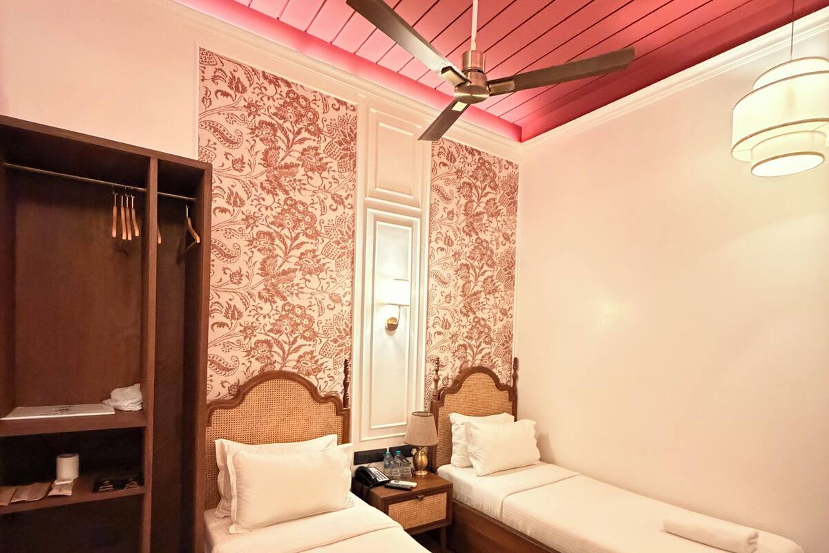 A hotel room with two single beds, a wardrobe, a ceiling fan, and a patterned wallpaper.