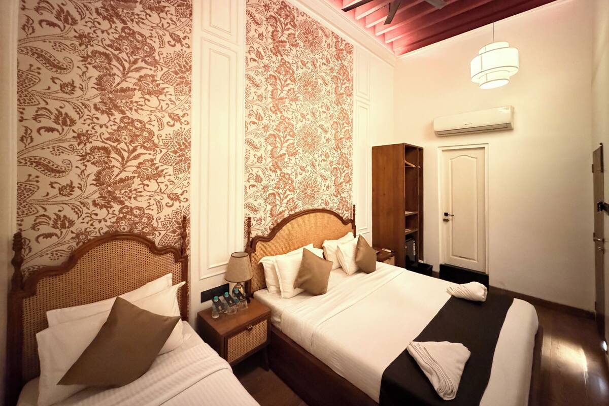 A hotel room with a large bed, a wooden wardrobe, a nightstand with a lamp, and a ceiling fan.