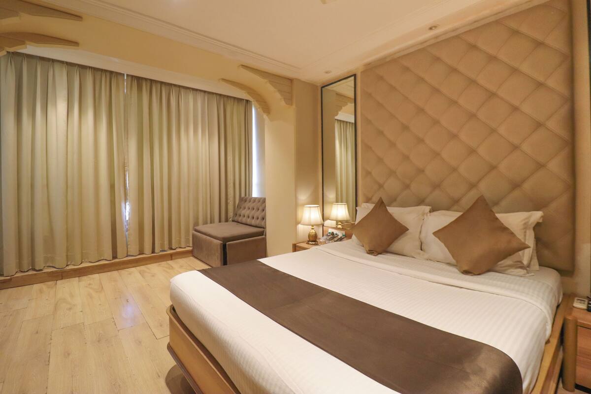 A hotel room with a large bed, a sitting area, a mirror, and a window with curtains.