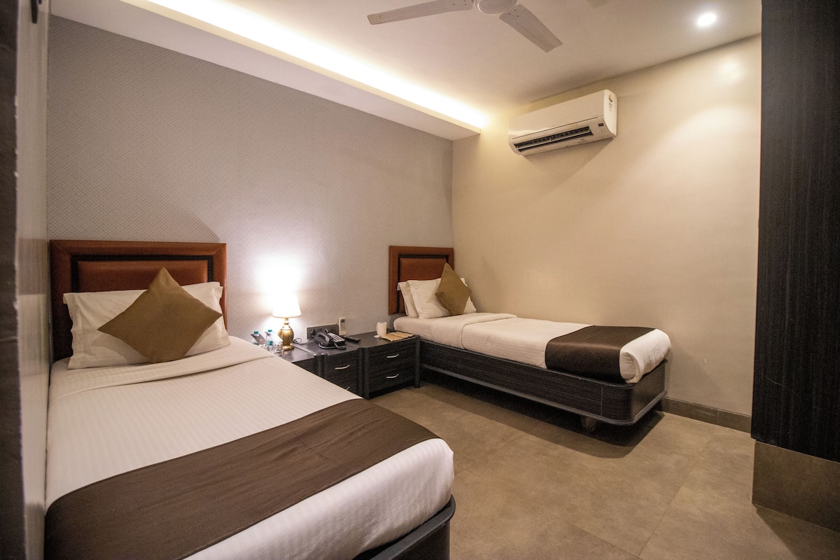 A hotel room with two beds, a nightstand, an air conditioning unit, and a ceiling fan.